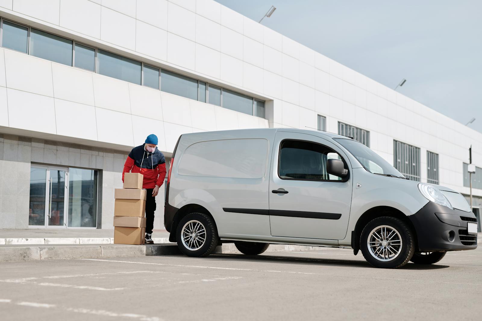 commercial auto A delivery driver wearing a face mask unloads packages from a van outside a modern building.